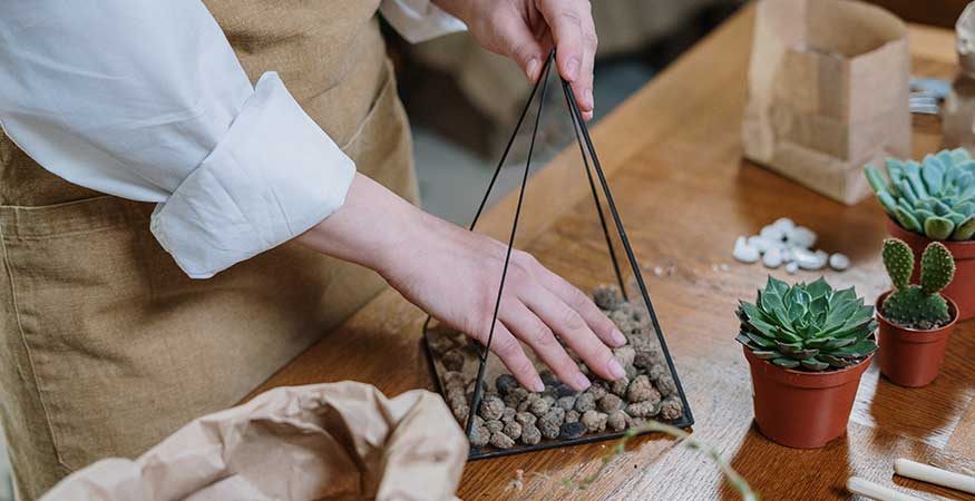 woman adding rocks to the bottom of a triangular plant terrarium